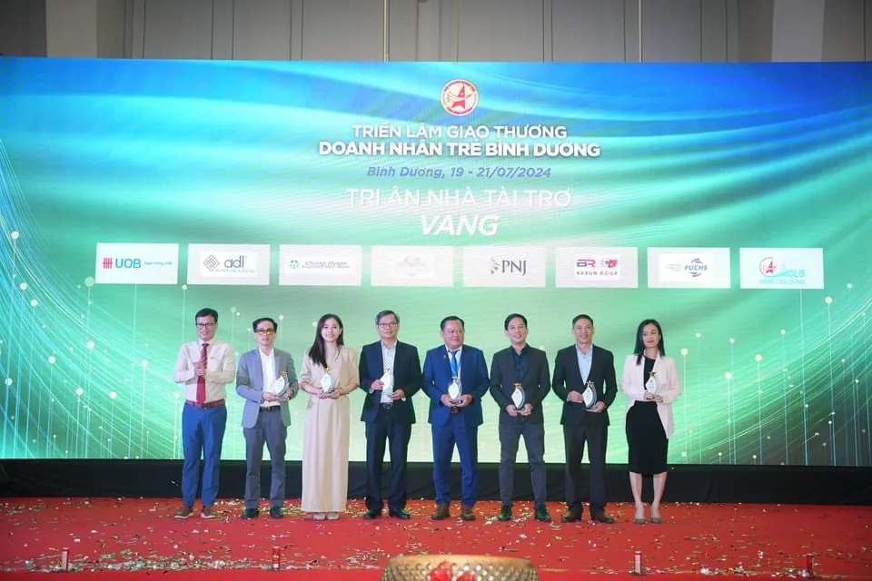 Đại diện các doanh nghiệp tài trợ Vàng cầm kỷ niệm chương trên sân khấu, phía sau là màn hình tri ân nhà tài trợ có logo Barun Door
