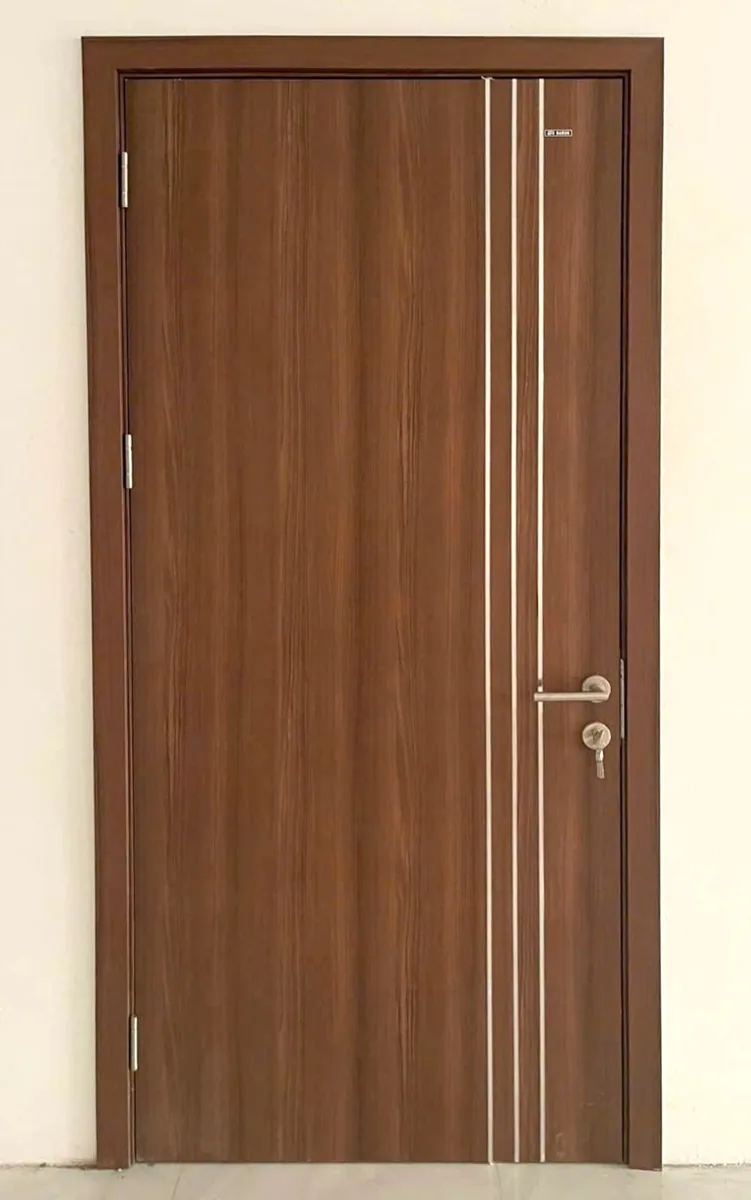 Cửa ABS v&acirc;n gỗ n&acirc;u c&oacute; ba đường chỉ dọc tr&ecirc;n c&aacute;nh, khung bao v&agrave; nẹp c&ugrave;ng m&agrave;u với c&aacute;nh, lắp ho&agrave;n thiện s&aacute;t tường