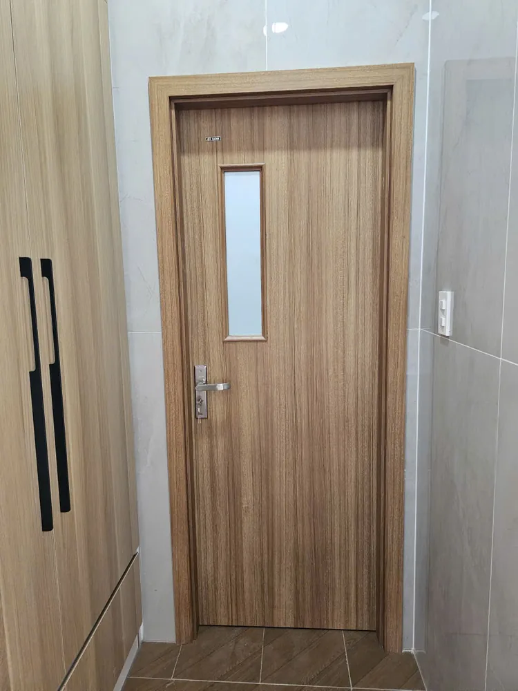 Cửa ô kính BR-K10 vân gỗ có ô kính dọc nhỏ, lắp tại khu vực ốp gạch dẫn vào phòng tắm
