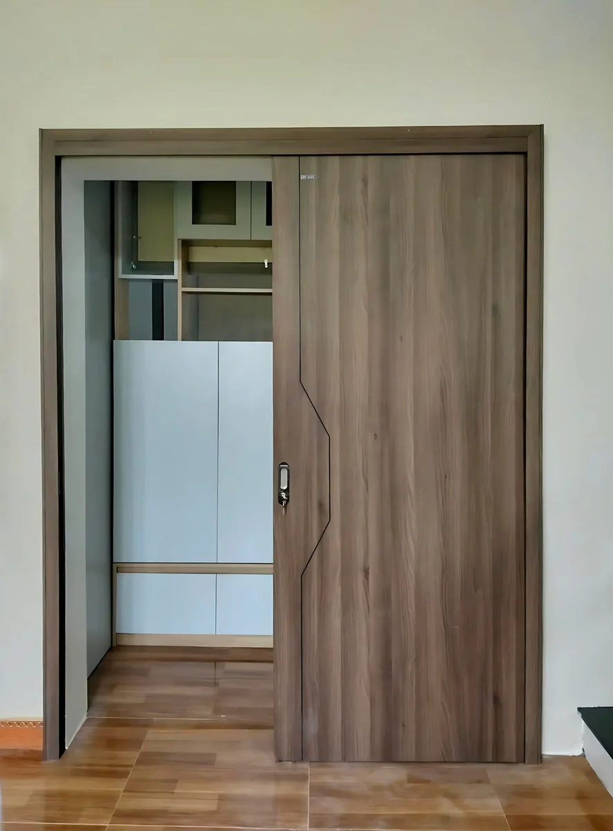 Cửa l&ugrave;a 1 c&aacute;nh ABS Barun Door v&acirc;n gỗ n&acirc;u c&oacute; đường CNC, mở một phần để lộ khu vực tủ ph&iacute;a sau