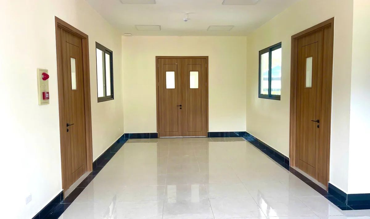 H&agrave;nh lang c&ocirc;ng tr&igrave;nh dịch vụ lắp cửa nhựa ABS v&acirc;n gỗ n&acirc;u, cửa đ&ocirc;i c&oacute; &ocirc; k&iacute;nh nhỏ ở cuối h&agrave;nh lang