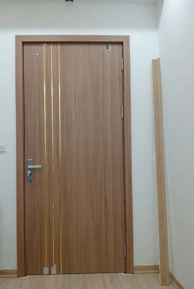 Cửa chỉ nh&ocirc;m v&acirc;n gỗ n&acirc;u s&aacute;ng với hai đường chỉ nh&ocirc;m v&agrave;ng chạy dọc c&aacute;nh, lắp tại c&ocirc;ng tr&igrave;nh thực tế