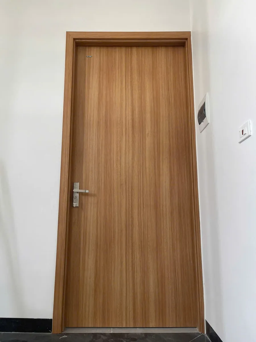 Cửa ph&ograve;ng ngủ trơn BR-100 v&acirc;n gỗ v&agrave;ng n&acirc;u, tay gạt inox, lắp trong căn hộ tường trắng
