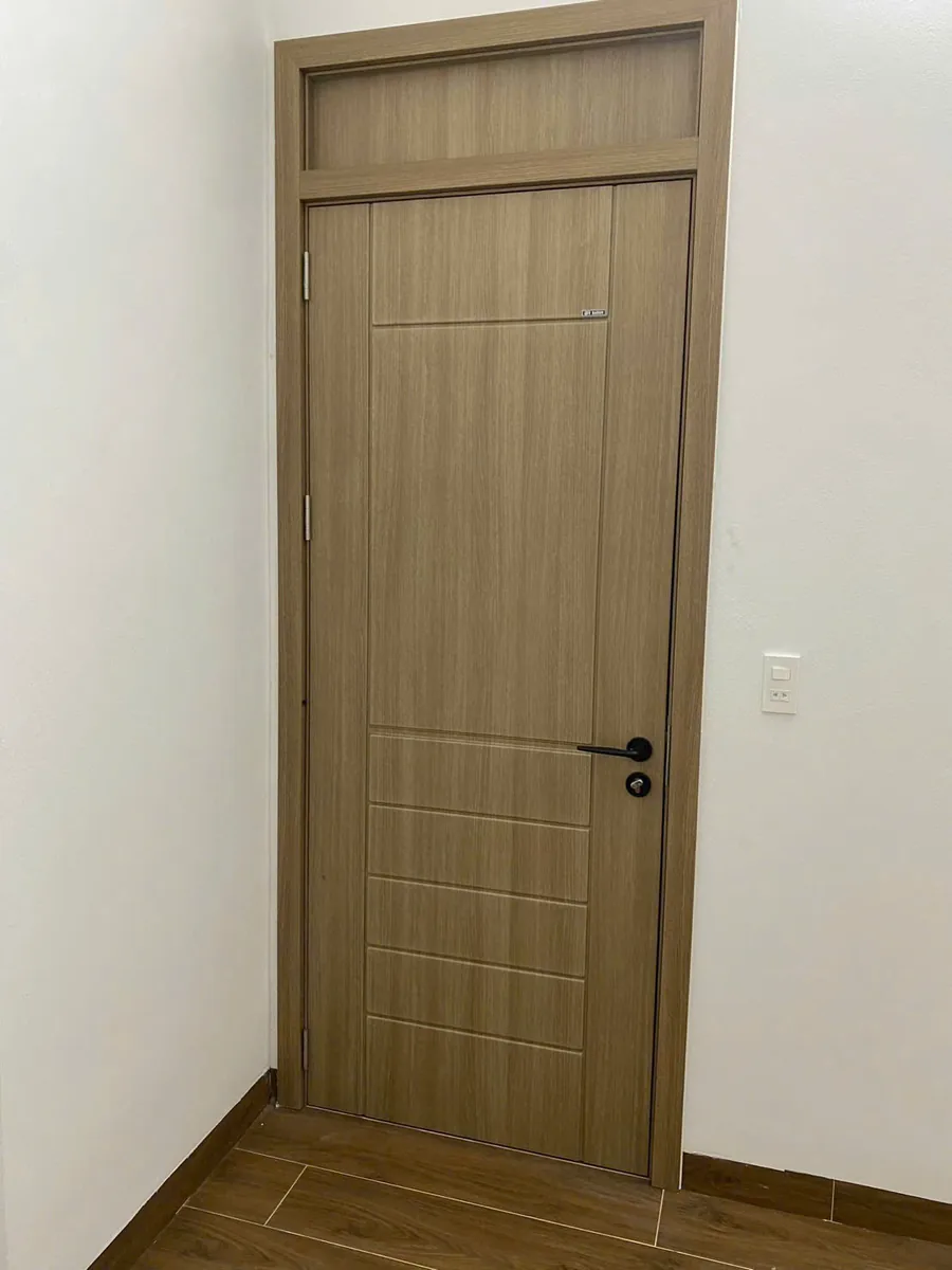 Cửa ABS v&acirc;n gỗ n&acirc;u nhạt c&oacute; &ocirc; fix tấm ABS c&ugrave;ng m&agrave;u ph&iacute;a tr&ecirc;n c&aacute;nh, khung bao chạy l&ecirc;n s&aacute;t trần, lắp tại c&ocirc;ng tr&igrave;nh