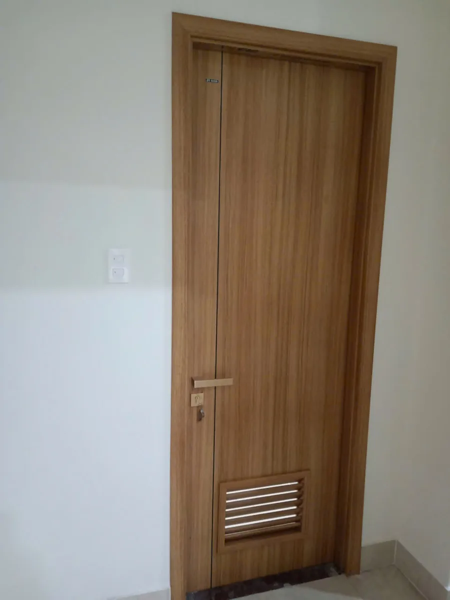 Cửa nhà vệ sinh ABS vân gỗ vàng có ô lam gió ở phần dưới cánh, lắp tại công trình thực tế