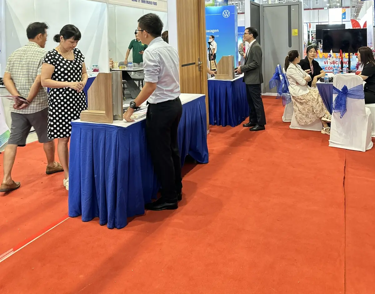 Nhân viên Barun giới thiệu mẫu mặt cắt khung cửa ABS cho khách tham quan tại bàn tư vấn trải khăn xanh, thảm đỏ triển lãm