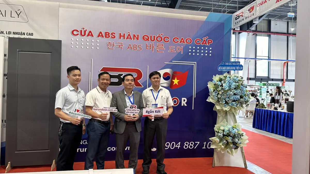 Bốn khách mời cầm bảng check-in Barun Door đứng trước phông gian hàng tại triển lãm
