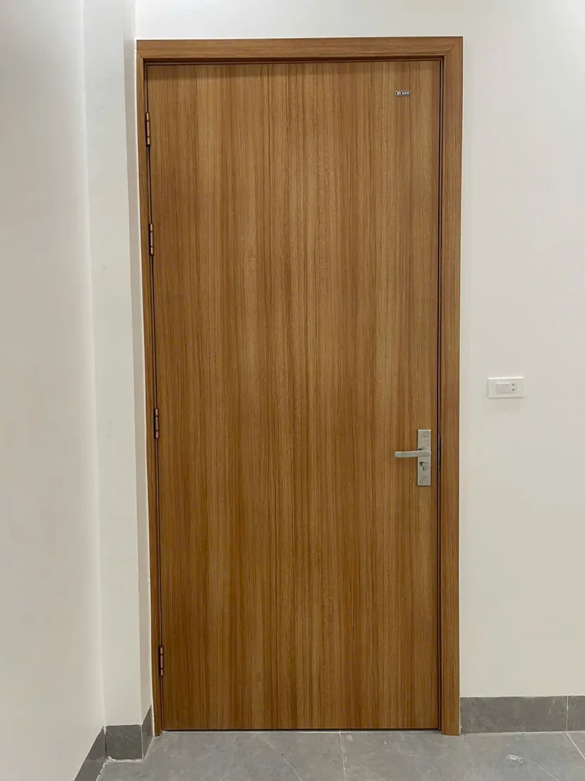 Cửa ABS trơn BR-100 v&acirc;n gỗ v&agrave;ng lắp trong ph&ograve;ng tường trắng, khung bao c&ugrave;ng m&agrave;u c&aacute;nh, tay gạt inox