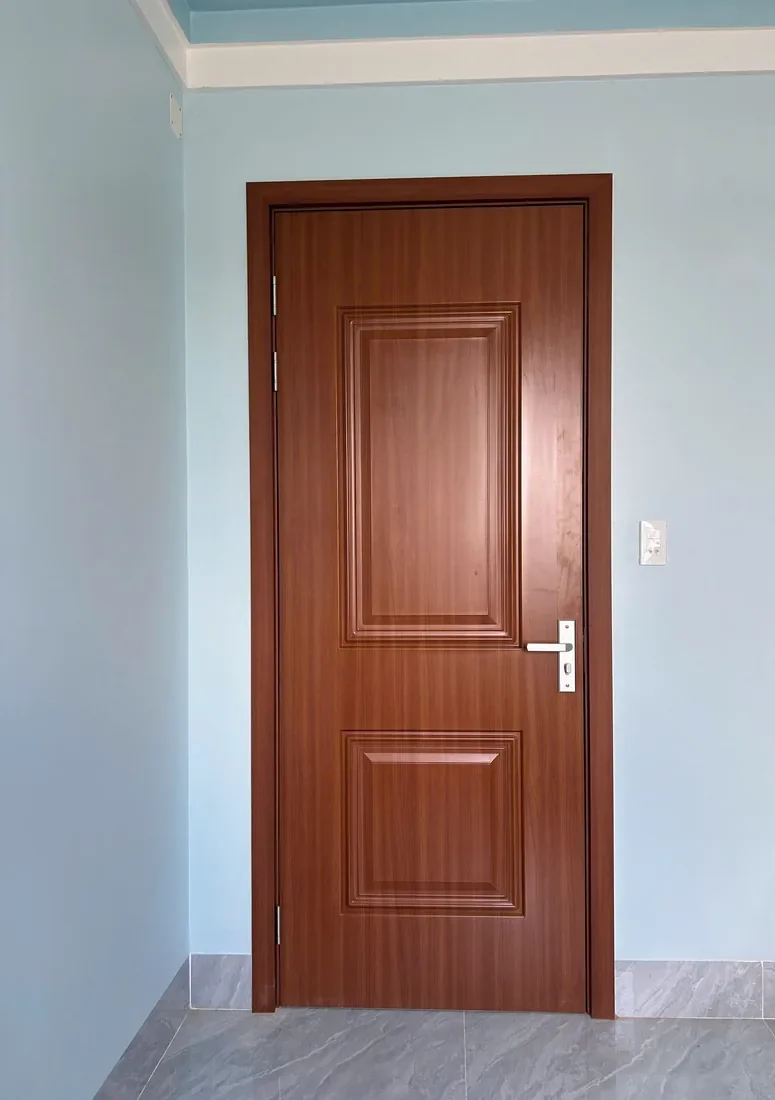 Cửa huỳnh ABS v&acirc;n gỗ n&acirc;u đỏ với hai &ocirc; huỳnh chữ nhật tr&ecirc;n c&aacute;nh, lắp trong ph&ograve;ng tường xanh nhạt